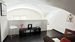 Un salon moderne avec un canapé blanc, un canapé rouge et marron, un fauteuil blanc, une console noire et un tableau encadré accroché au mur.