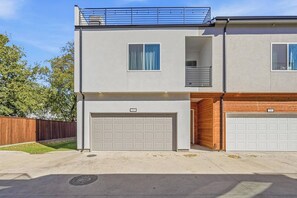 A two-story residential building with a garage, a balcony, and a small enclosed porch. - Modern 3BR Home w/ Rooftop • 5 min to Downtown (Dallas)