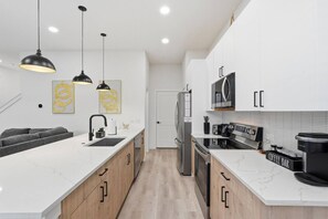 A modern kitchen with white cabinetry, a marble countertop, a built-in oven, a coffee machine, and pendant lighting. - Modern 3BR Home w/ Rooftop • 5 min to Downtown (Dallas)