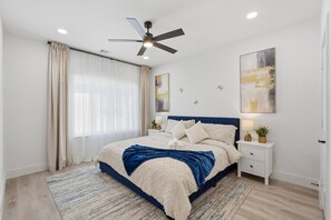 A bedroom with a bed, a nightstand, a ceiling fan, a window with curtains, and artwork on the wall. - Modern 3BR Home w/ Rooftop • 5 min to Downtown (Dallas)