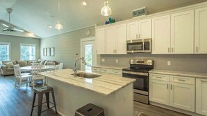 A modern kitchen with white cabinets, a central island, a microwave, and a stove. - Sea Breeze Two - Pet Friendly - New Eastpoint (Eastpoint)