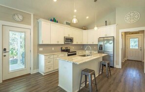 Una cocina moderna con armarios blancos, una isla central, electrodomésticos de acero inoxidable e iluminación colgante.