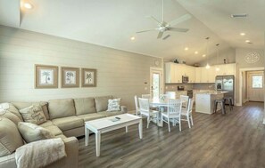A spacious living area with a sofa, coffee table, and dining set. There is a kitchen with white cabinets and a refrigerator. - Sea Breeze Two - Pet Friendly - New Eastpoint (Eastpoint)