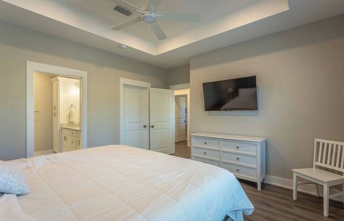 Une chambre à coucher avec un lit, une commode, une télévision et un ventilateur de plafond.