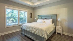 A bedroom with a bed, two bedside tables, a ceiling fan, and large windows. - Sea Breeze Two - Pet Friendly - New Eastpoint (Eastpoint)