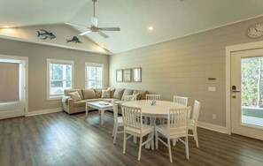 A spacious living area with a dining table, white chairs, a sofa, and a ceiling fan.