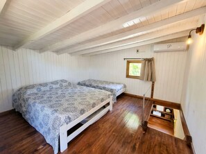Un dormitorio con dos camas, suelo de madera, una ventana con cortinas y una pequeña estantería con objetos.