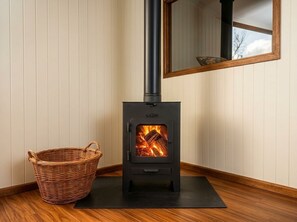 A wood-burning stove with a fire, a wicker basket, and a mat on the floor. - Nature and Exclusivity | Premium (Provincia de Buenos Aires)