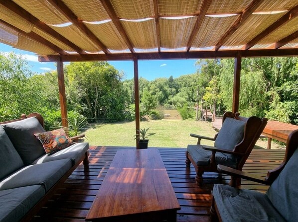 Un espacio de estar al aire libre cubierto con vistas a un jardín exuberante y una mesa de madera.