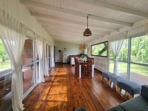 A spacious room with wooden flooring, a dining area with a table and chairs, and large windows with curtains. - Nature and Exclusivity | Premium (Provincia de Buenos Aires)