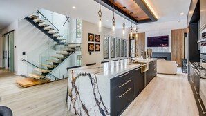 A modern kitchen with a marble island, a glass staircase, and a large window. - Serenity Estates in South Fulton (Atlanta)