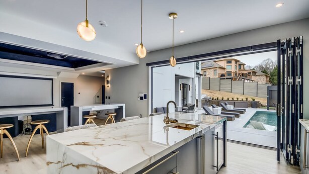 A modern kitchen with a marble island, pendant lighting, and a view of a swimming pool. - Serenity Estates in South Fulton (Atlanta)