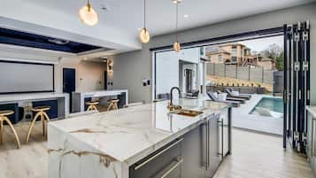 A modern kitchen with a marble island, pendant lighting, and a view of a swimming pool.