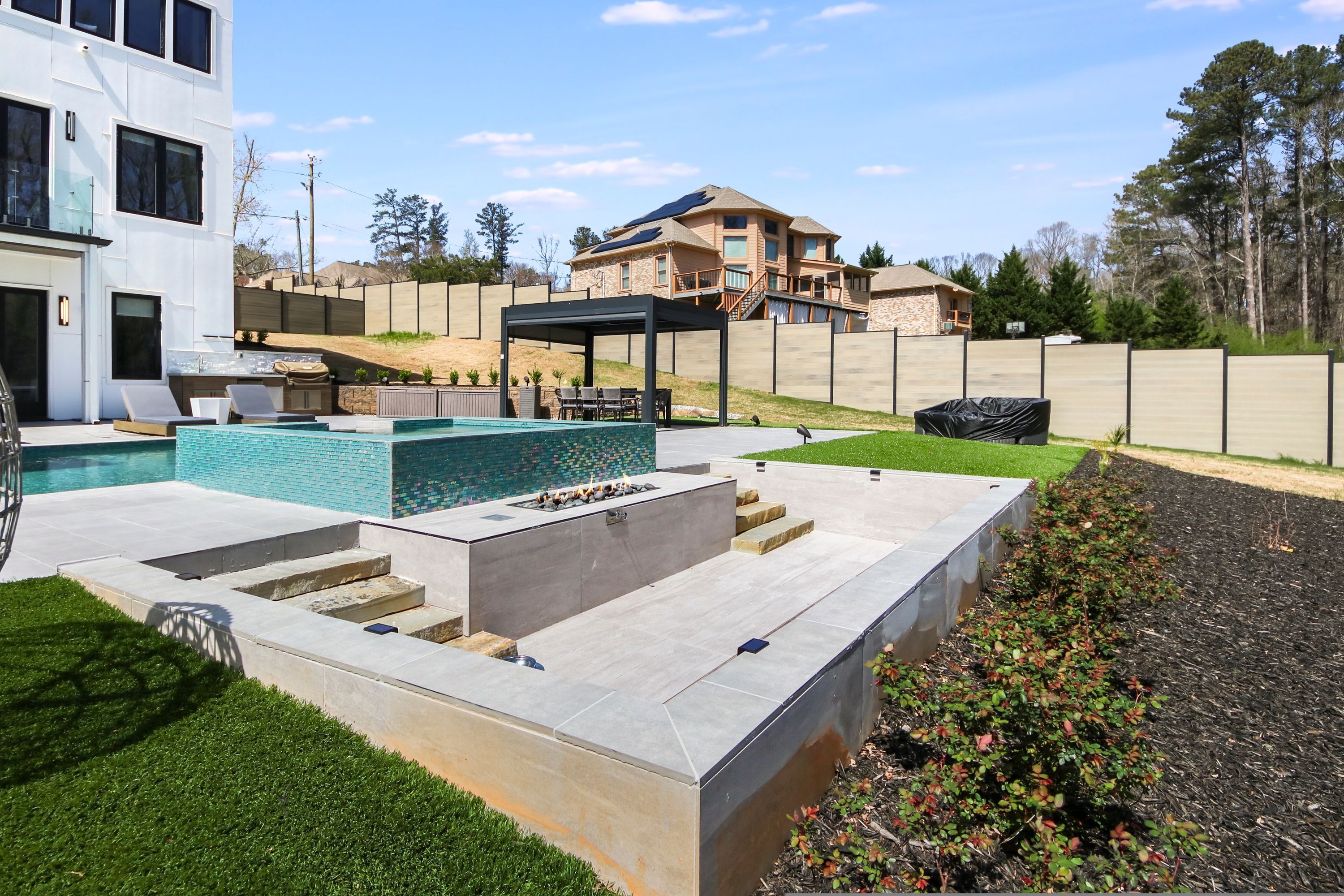 A modern outdoor pool area with a pergola, a barbecue, and a stone patio.