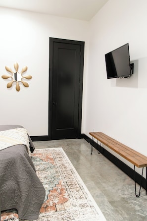 Un dormitorio con cama, una banca, televisor y puerta.