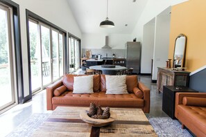 Amplia sala de estar con un sofá de cuero marrón, una mesa de centro de madera y un ventanal con vistas al exterior.