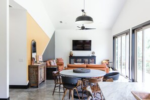 A modern living room with a dining area, a ceiling fan, and a large window.