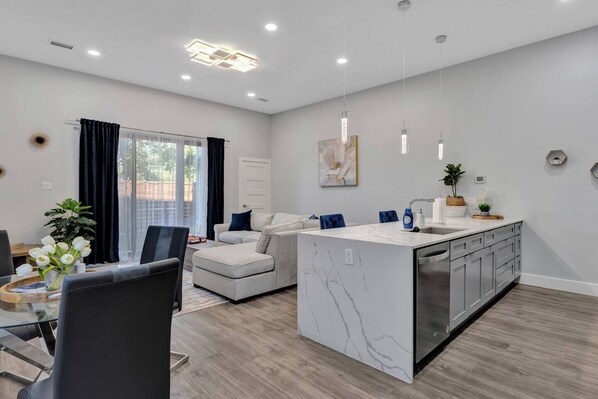 A modern kitchen with a marble island, a dining area with a table and chairs, and a living room with a sofa and a coffee table. - Entire Duplex Unit · Cozy, Bright & Fully Equipped (Dallas)