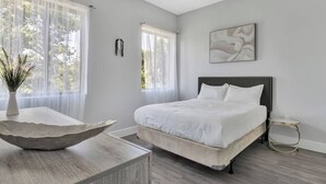 Ein Schlafzimmer mit einem Bett, einer Pflanzvase, einem Gemälde und einem Fenster mit transparenten Vorhängen.