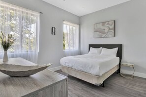 A bedroom with a bed, a vase with plants, a painting, and a window with sheer curtains. - Entire Duplex Unit · Cozy, Bright & Fully Equipped (Dallas)