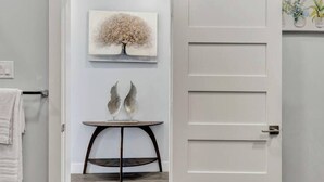 Ein Zimmer mit einer weißen Tür, einem gerahmten Kunstwerk darüber und einem kleinen Tisch mit Dekorationen.