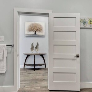 A room with a white door, a framed artwork above it, and a small table with decorative items. - Entire Duplex Unit · Cozy, Bright & Fully Equipped (Dallas)