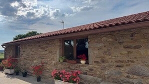 A stone building with a tiled roof, windows with potted plants, and a clear sky.