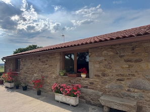A stone building with a tiled roof, windows with potted plants, and a clear sky.