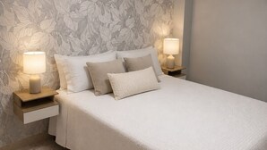 A bedroom with a bed, two bedside lamps, a nightstand, and a floral-patterned wallpaper.