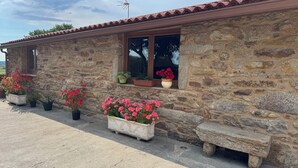 A stone building with a tiled roof, a window with a potted plant, and a stone bench.