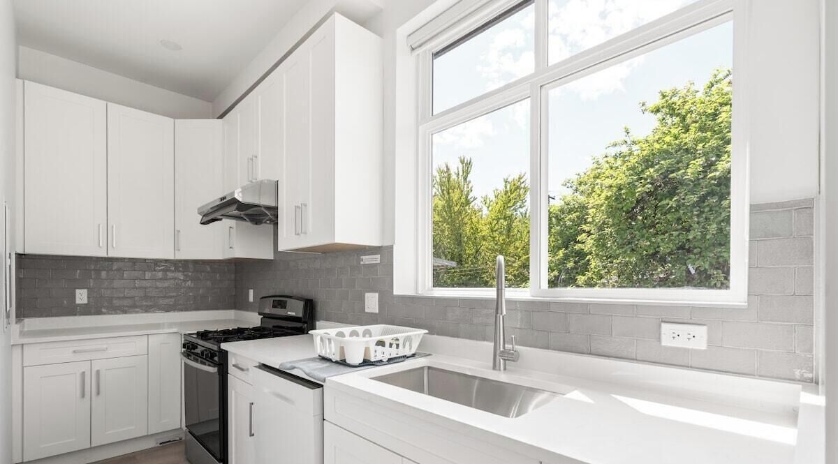 A modern kitchen with white cabinetry, a stove, and a large window offering a view of trees.
