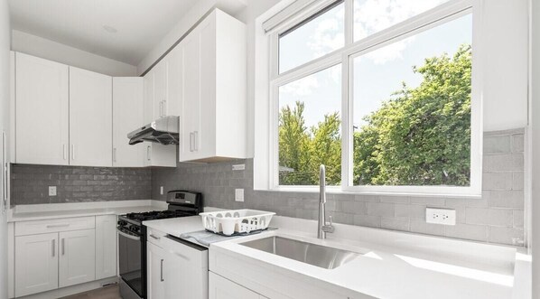 Eine moderne Küche mit weißen Schränken, einem Herd und einem großen Fenster mit Blick auf Bäume.