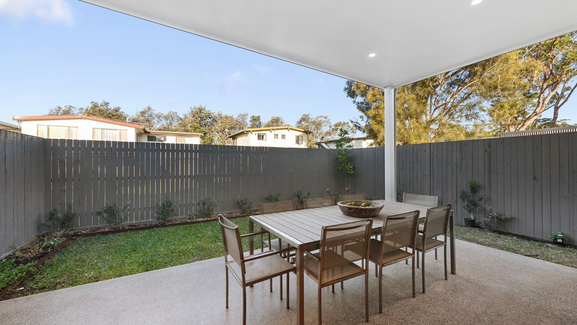 A patio with a table and chairs, surrounded by a wooden fence and a grassy area.
