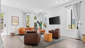 Una sala de estar moderna con un sofá, dos sillones, una mesa de centro y un televisor de pantalla plana montado en la pared.