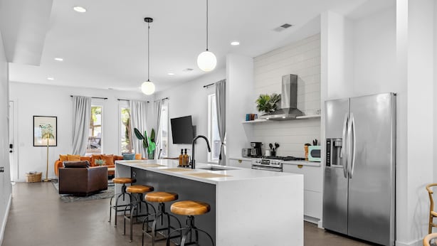 Una cocina moderna con una isla central, electrodomésticos de acero inoxidable y una zona de comedor con taburetes de bar.