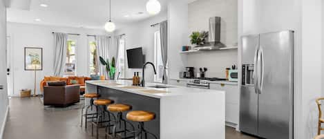 Et moderne køkken med en central ø, rustfrstål-hvidevarer og et spiseområde med barstole.
