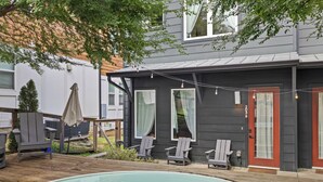 Una propiedad residencial con piscina, sillas de deck y una casa de exterior oscuro y puerta roja.