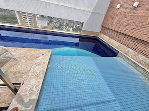 Une piscine dont les bords sont recouverts de carreaux, une chaise en métal et un mur en briques.