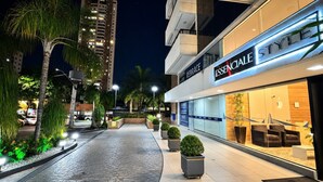 Un bâtiment moderne avec une enseigne indiquant « ESSENCIALE STYLE » et un trottoir dallé agrémenté de jardinières.