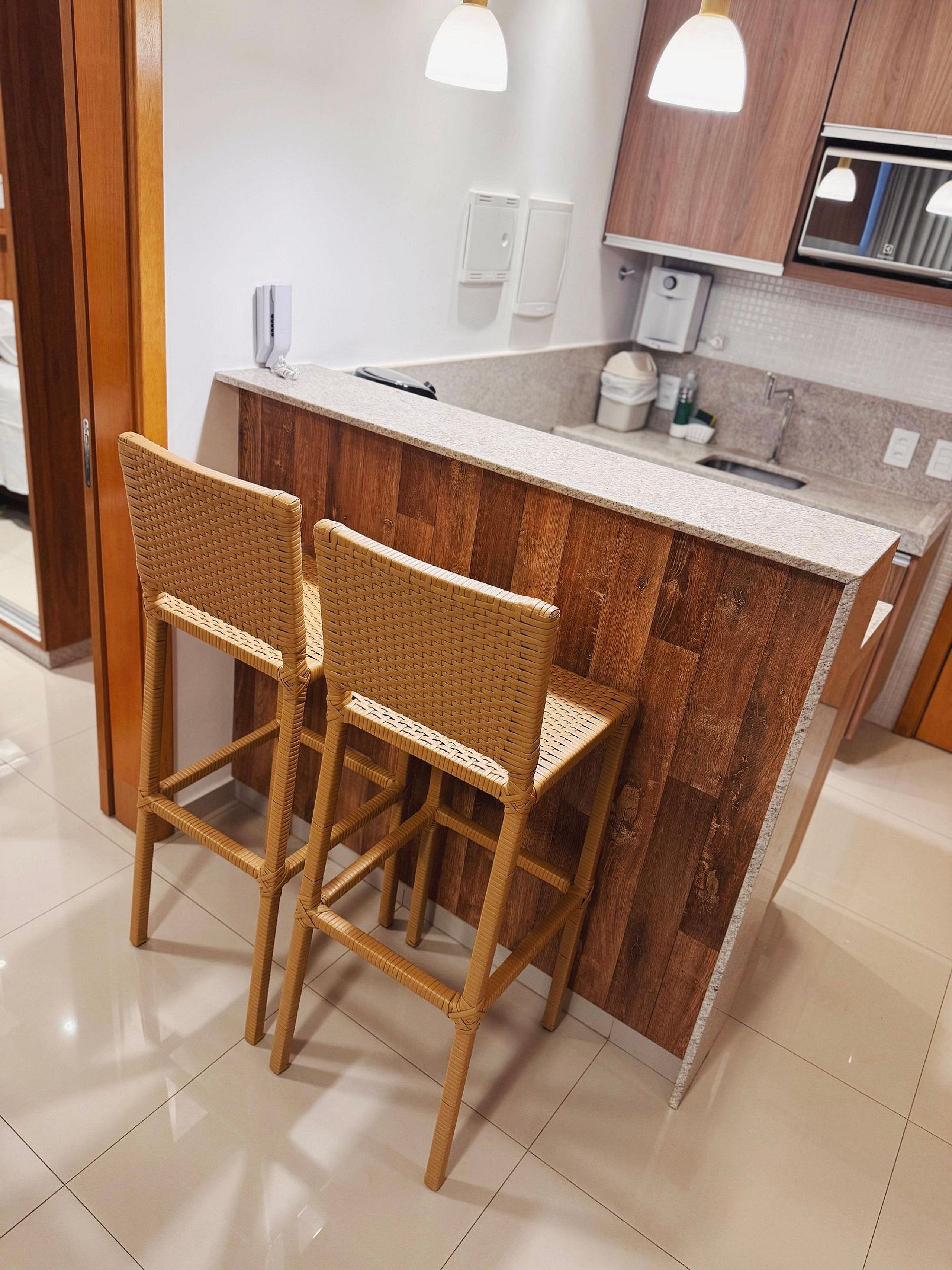 Una cocina con una isla de madera, dos taburetes de mimbre e iluminación colgante.