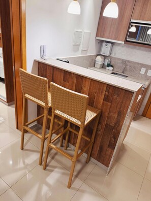A kitchen with a wooden island, two wicker bar stools, and pendant lighting.