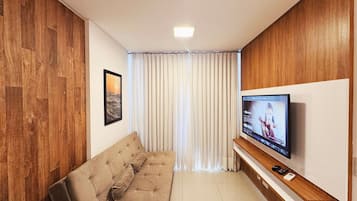 A modern living room with a wooden panel wall, a beige sofa, a mounted TV, and a framed picture on the wall.
