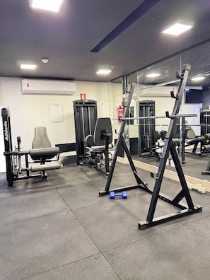 A gym with exercise equipment, a mirror, and a wall-mounted air conditioning unit. - Essencialle Style 1Q (Goiânia)