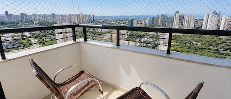 A balcony with two wicker chairs, a metal railing, and a city view.