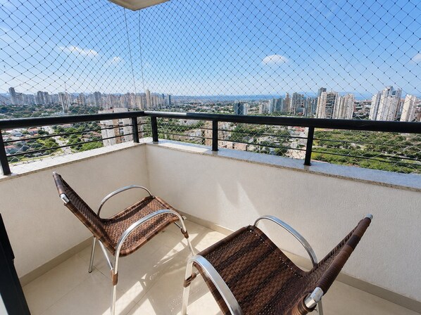 A balcony with two wicker chairs, a metal railing, and a city view.