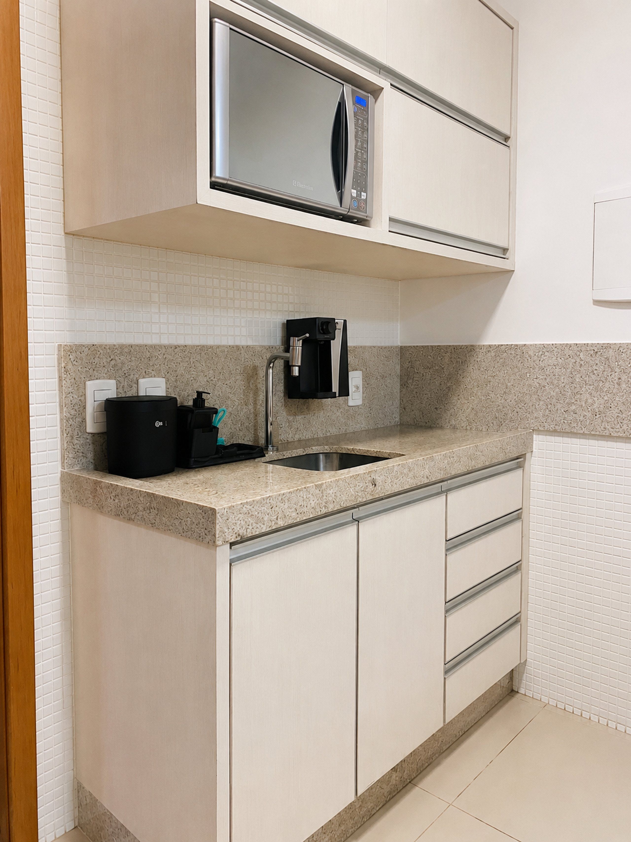 A kitchen with a built-in microwave, coffee machine, and a stainless steel sink.