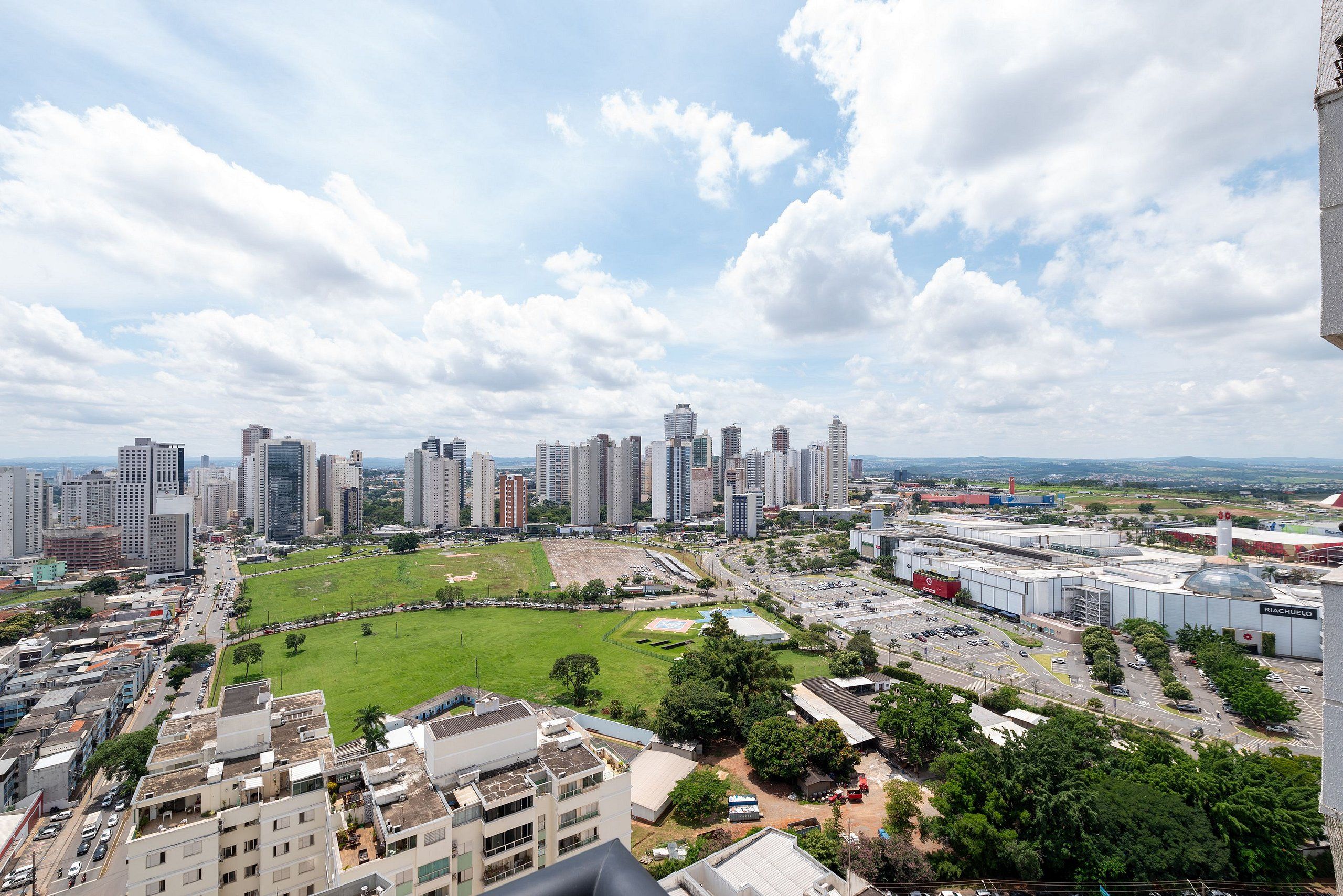 A cityscape with high-rise buildings, a large open green space, and a parking area.