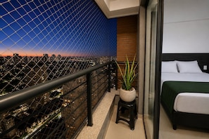 Un balcon avec vue sur la ville, une plante en pot et un lit recouvert d’une couverture verte.