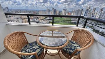 A balcony with wicker chairs and a glass table, overlooking a cityscape with high-rise buildings.