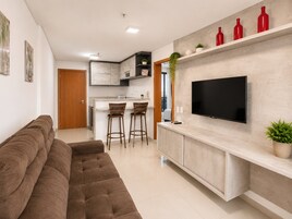 Una sala de estar moderna con un sofá, un televisor montado en un mueble y una zona de cocina con taburetes.